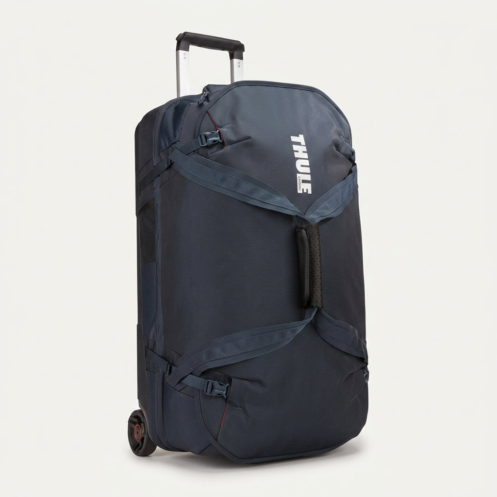 A navy blue Thule rolling duffel bag with an extended telescoping handle and wheels, shown from a three-quarter angle against a light off-white background.