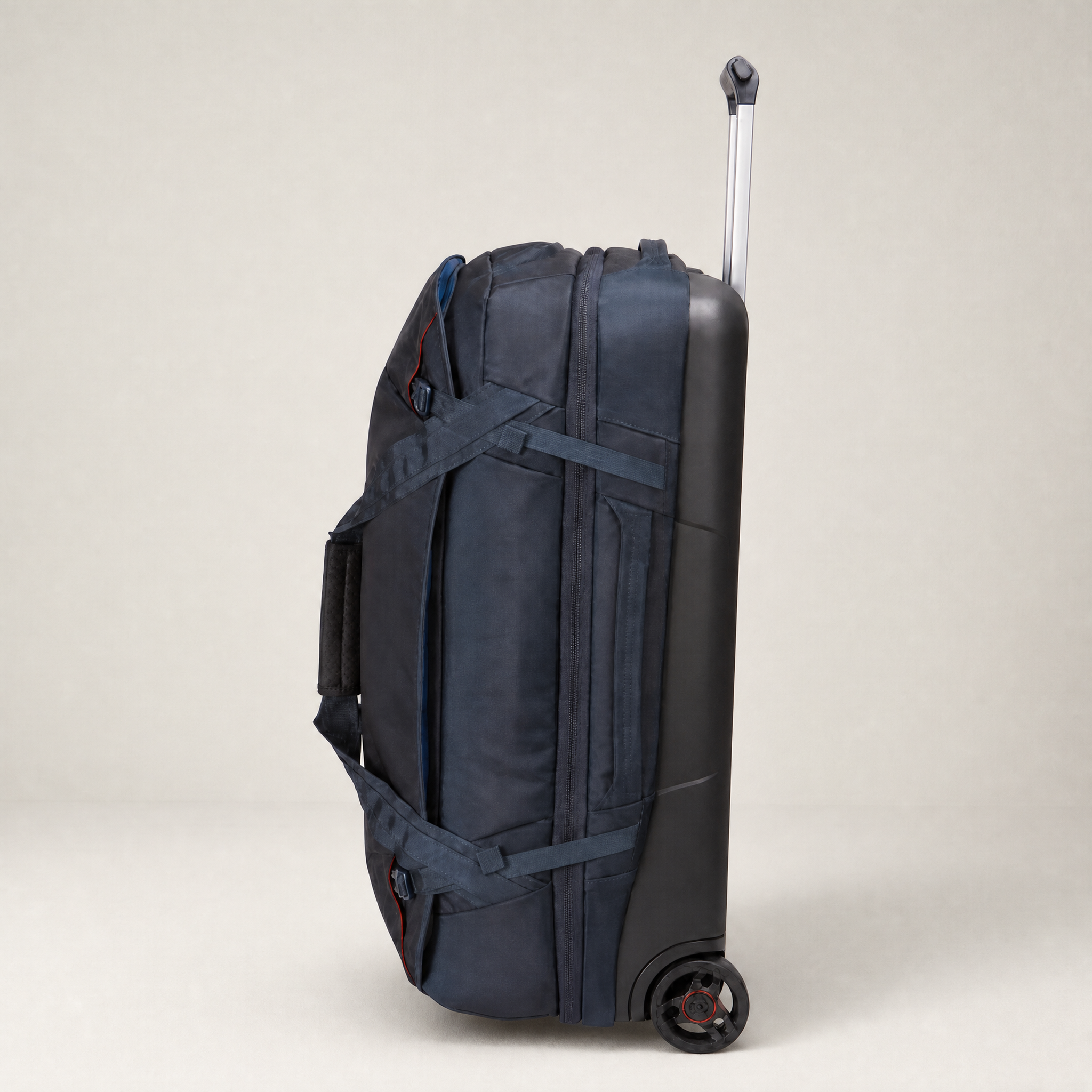 A navy blue rolling duffel bag with an extended telescoping handle and side compression straps, shown from a side profile against a neutral light beige background.